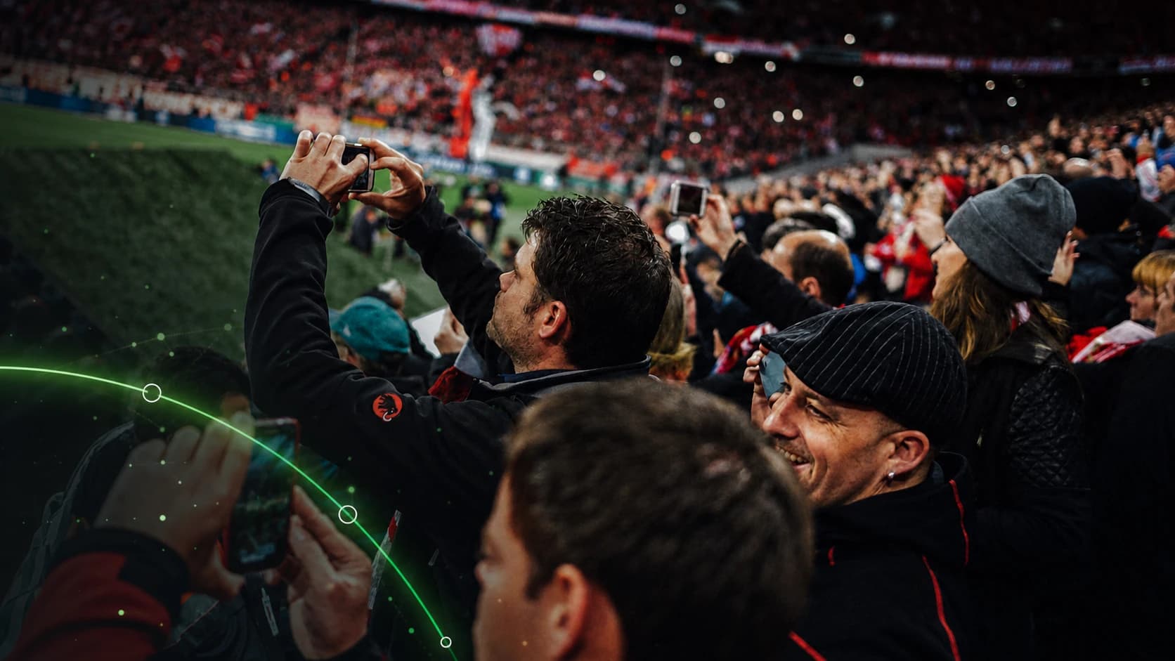 Football supporters check their phones from inside a packed stadium.