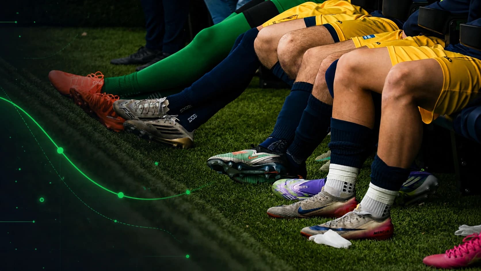 Adult football substitutes in full match kit sit together in the technical area.